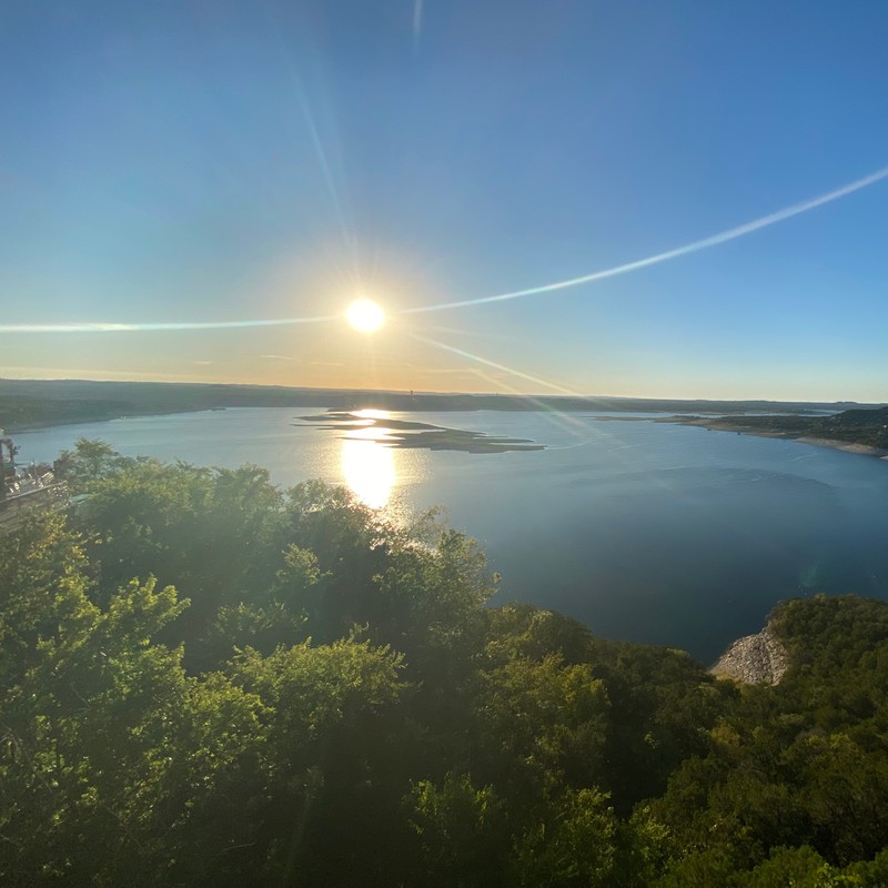 a body of water with trees around it and the sun in the sky