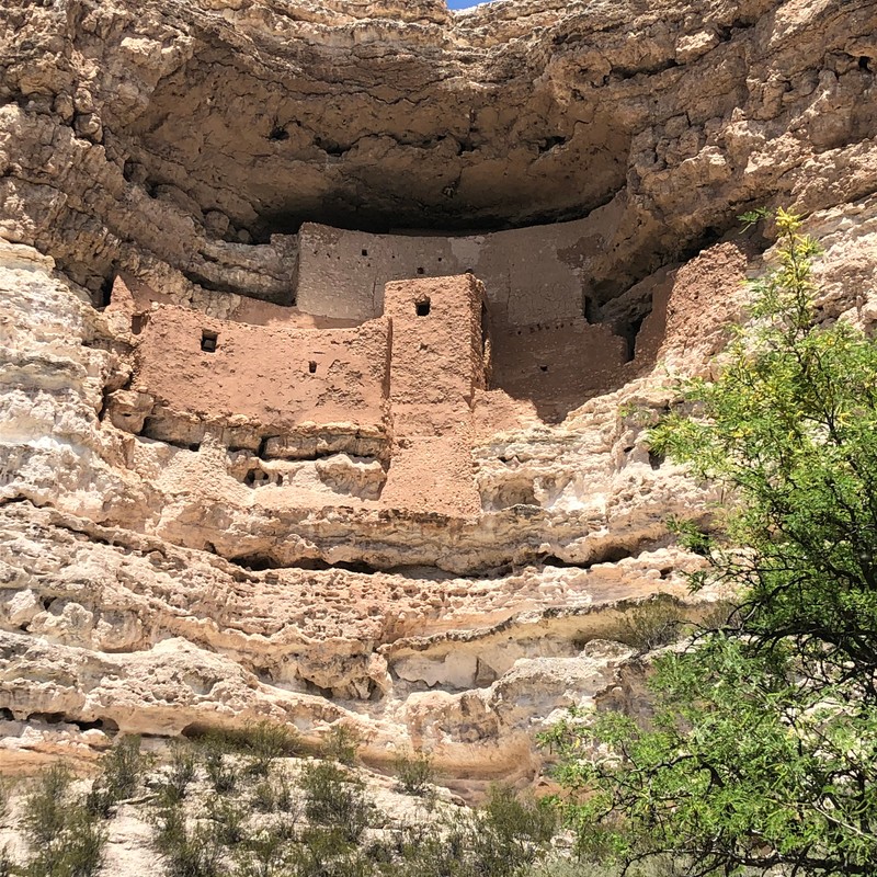 a rock cliff with a hole in it with Montezuma Castle National Monument in the background