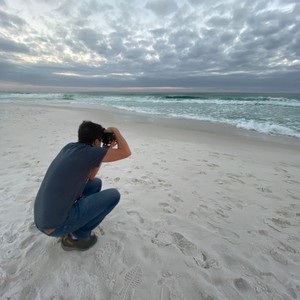 a man kneeling on a beach taking a picture of the ocean