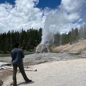 a man holding a stick looking at a large geyser