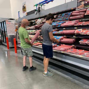 a couple of men standing in a store with a shelf of meat