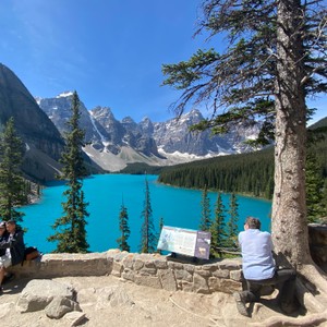 a man sitting on a rock by Moraine Lake with mountains in the background