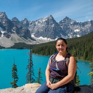 a person sitting on a rock by a lake with mountains in the background