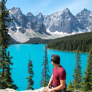 a man sitting on a rock overlooking a lake and mountains