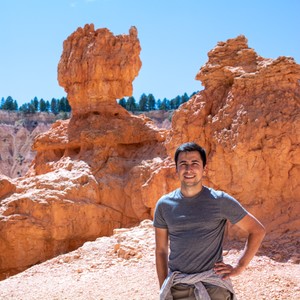 a man posing in front of a large rock formation