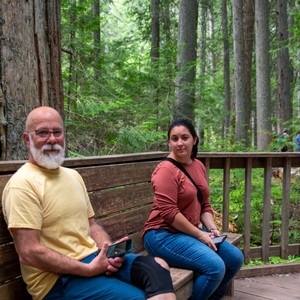 a man and woman sitting on a bench in the woods