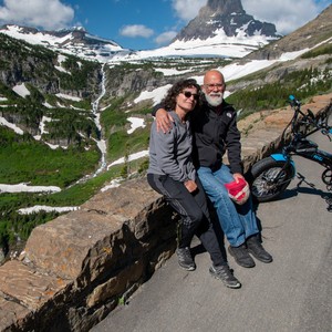 a man and woman sitting on a rock with a mountain in the background