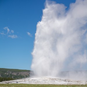 a large geyser in a field with Old Faithful in the background